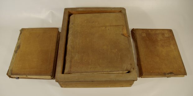 Set of Altar Books found in St. James. The covers are light brown worn leather. The Gospel Book is inside a simple box while the Communion book and Prayer book sit on either side of Gospel.