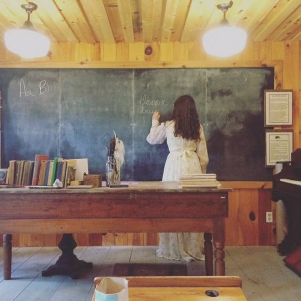 A teacher writes on a blackboard in an wooden house