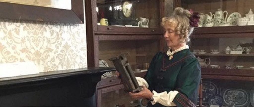 A woman dressed in a period costume (late 1800s) holds a small easel