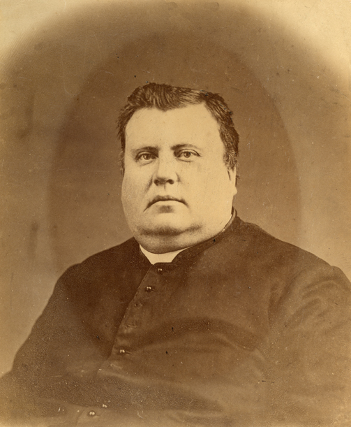 Sepia-tone photograph of a priest in his forties. The portrait shows his upper body; he is portly, with a double chin. He wears a cassock and clerical collar.