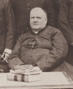 Black & white photograph of Curé Labelle. He is seated and, with his cassock unbuttoned and opened at the chest, his excess weight is conspicuous.