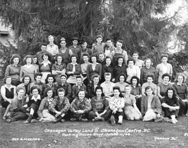 Black and white photo of 36 women and 10 men outside, arranged in four rows - two seated and two standing - with the men in the back row. A large evergreen tree is behind them.