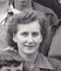 Black and white head photo of a young woman smiling at the photographer. Her curly hair is combed back.