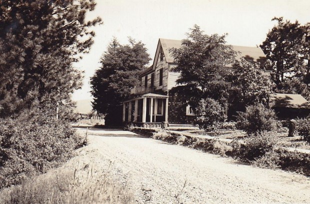 Black and white photo of a wooden house on an unpaved road.