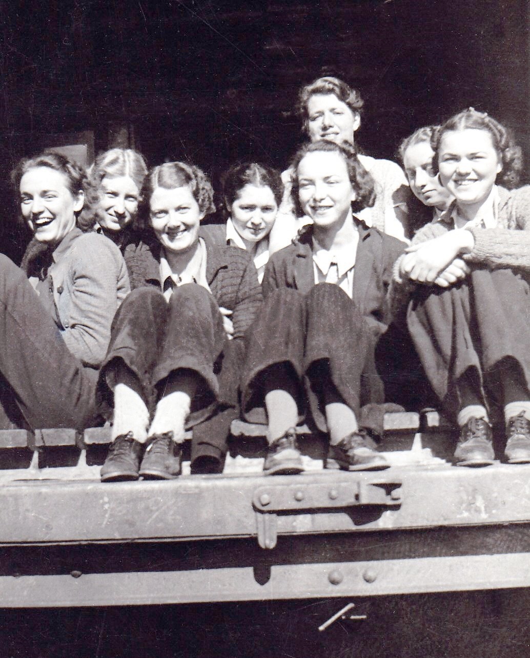 Black and white photo of eight women sitting in the doorway of a loading dock.