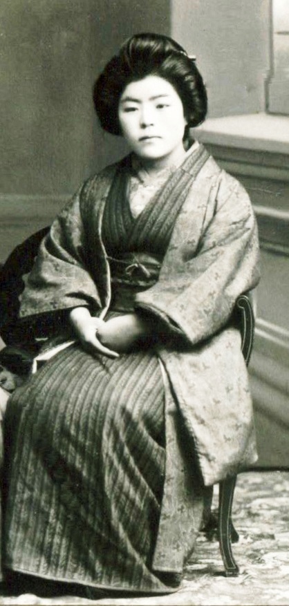 Black and white photo of a seated young woman. She is wearing traditional Japanese formal dress.