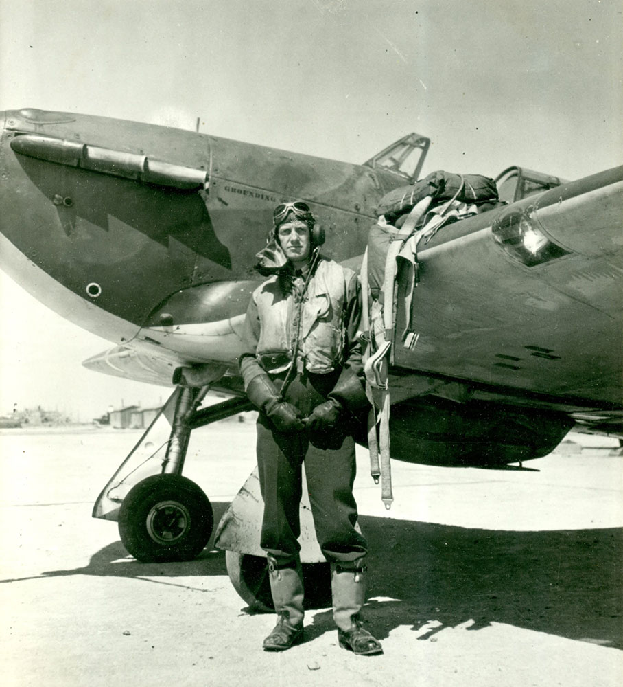 A black and white photo of Lamont Parsons standing next to his Hawker Hurricane Fighter aircraft in his flight suit with parachute pack on wing.