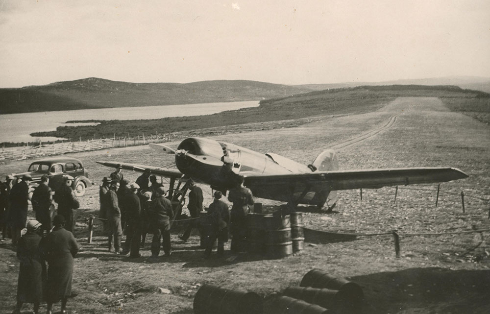 Black and white photograph of a small crowd gathered around the aircraft, the Dorothy, secured at airstrip.