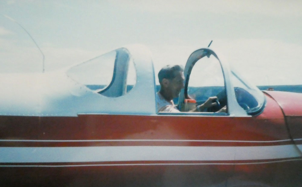 A colour photograph of Claude Stevenson sat in the cockpit of his red and white aircoupe.