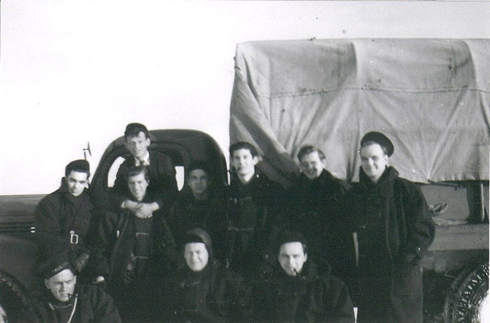 A black and white photograph of ten Navy Officers posing in front of a covered Navy truck.