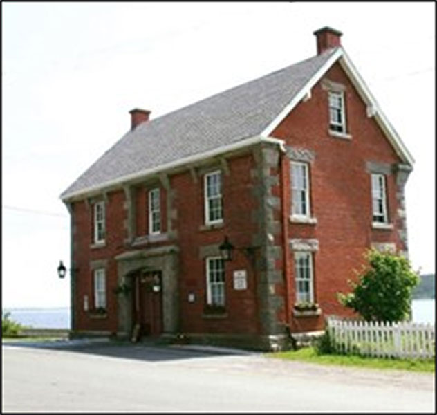 A coloured photo of an historic brick building on side of road.