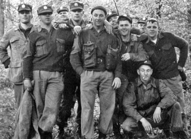 Group of ten soldiers pose for outdoor photo in a wooded area