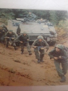 Al Murphy and other soldiers on training exercises. Soldiers with weapons move in formation in front of an army tank.