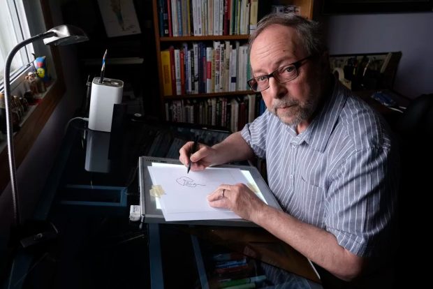 Photo of caricaturist Guy Badeaux at his drawing desk.