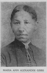 black and white professional portrait, turned to face the camera, hair pulled back, wearing muted colored dress with high collar, broach with necklace