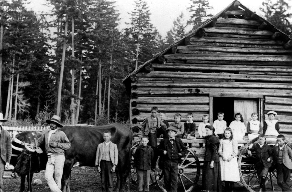 Bâtiment à un étage en bois rond. Au premier plan, un cheval et un chariot; les conducteurs et les enfants s’y tiennent devant