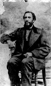 black and white professional studio portrait of middle-aged man seated, dark hair and trimmed dark beard, wearing formal suit