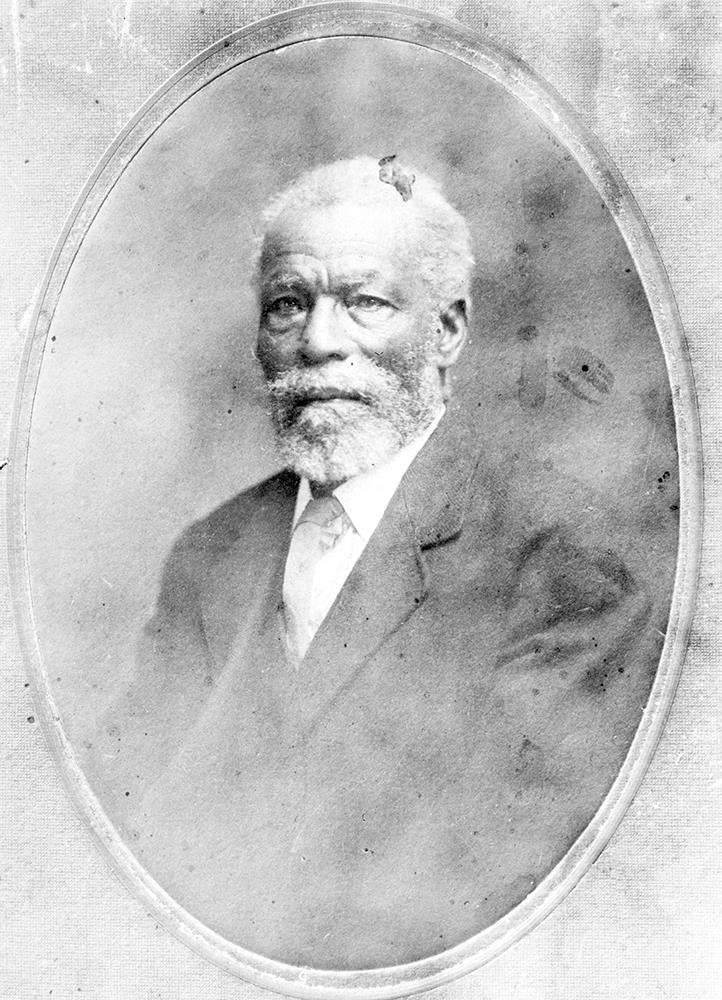 black and white professional studio portrait in oval frame, senior man with white hair and beard and moustache in formal suit and tie.