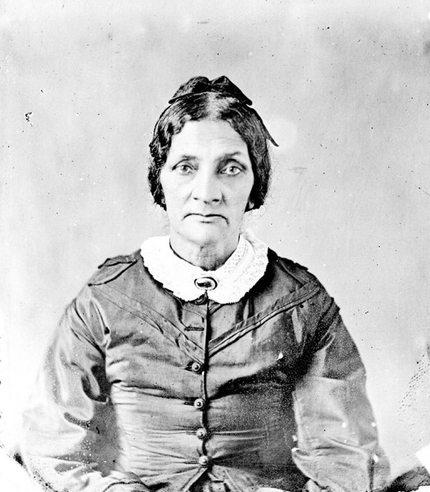 black and white professional portrait, facing the camera, hair pulled back, wearing muted colored dress with white collar held by a brooch