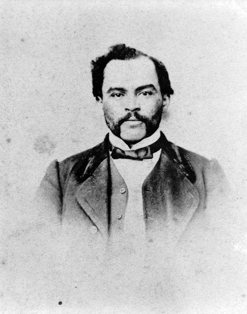 black and white professional studio portrait, man facing camera with dark hair, sideburns, in formal suit.