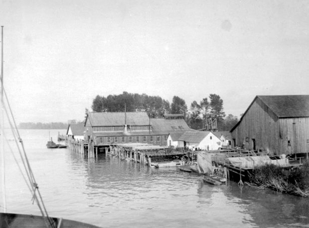several wooden buildings of various sizes and heights at docks on a river bank