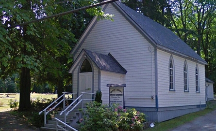 church with white clapboard siding, grey roof in treed setting. front steps to entryway.