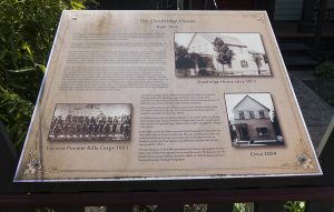 commemorative plaque with text and 3 images mounted on a fence at a slight angle visible to passersby