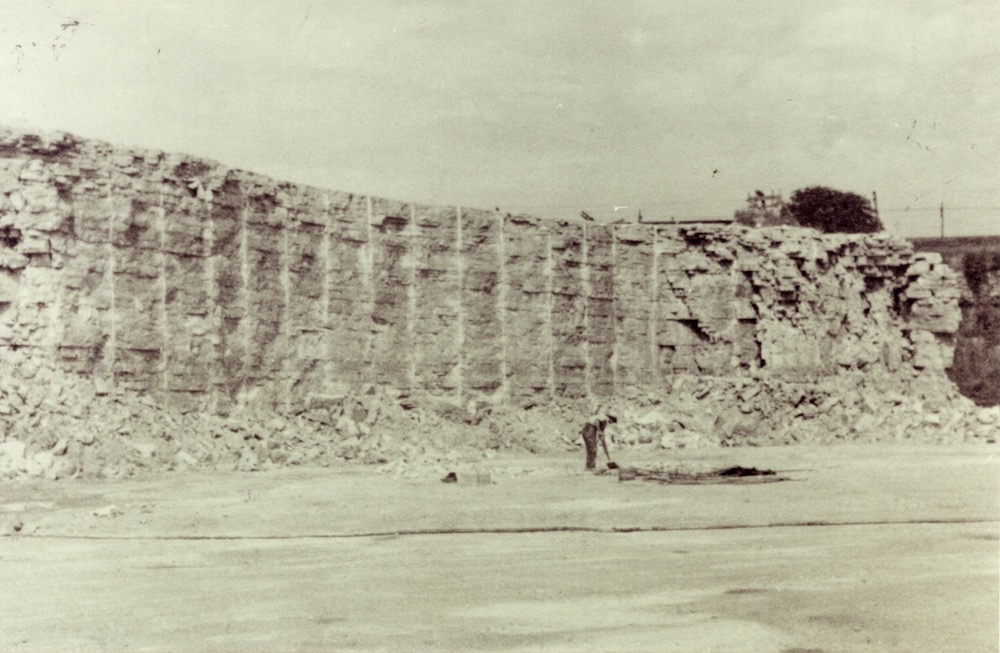 A man stands against the backdrop of a quarry wall that has vertical stripes running along it.