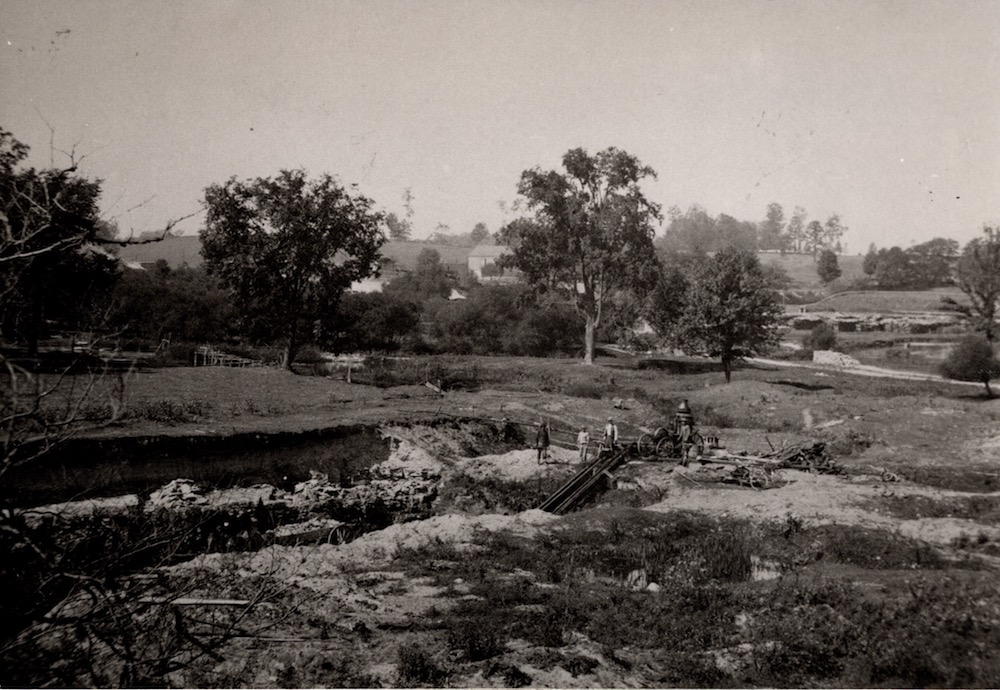 A group of workers standing on a rural landscape beside a pit in the earth