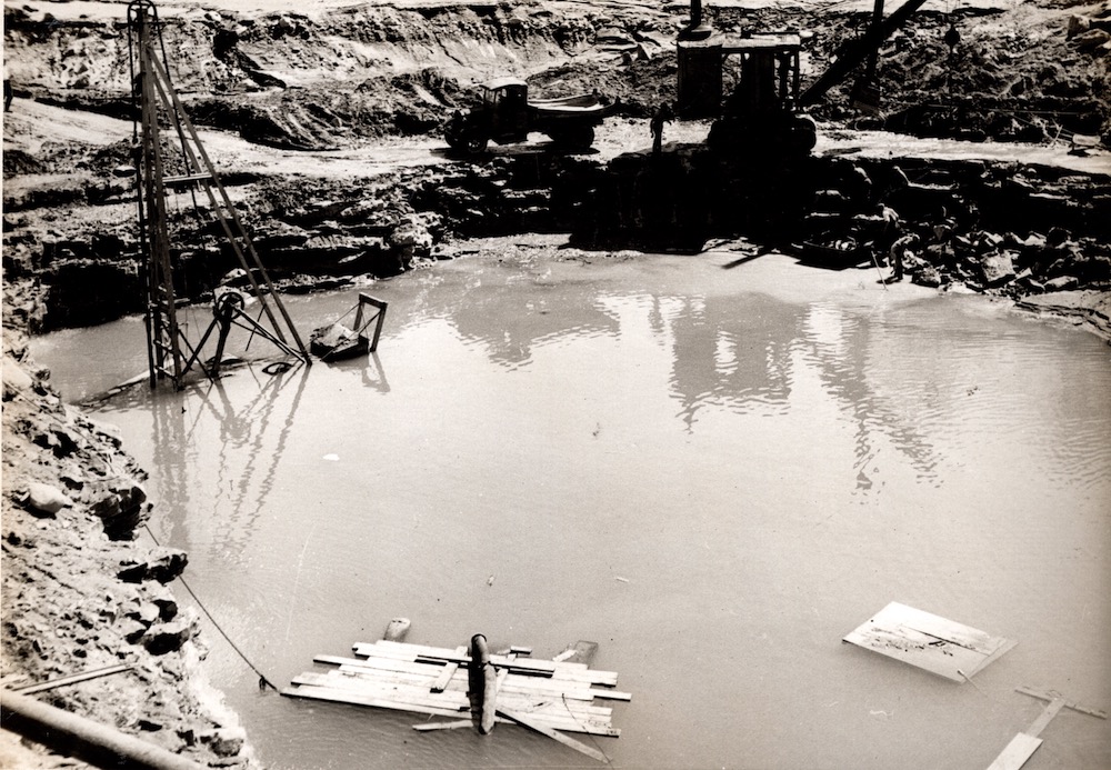 Water pooled in a quarry pit with pieces of equipment slightly visible above the water