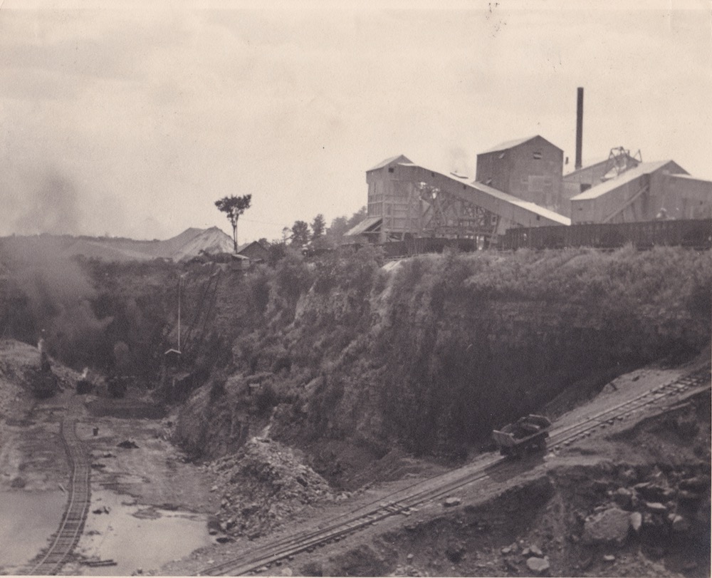 Un chariot avance sur une piste sur une rampe qui mène d'une fosse à un ensemble de bâtiments industriels.