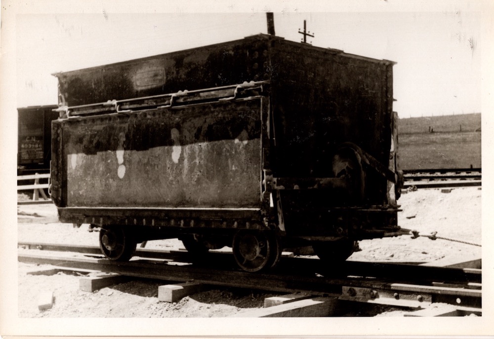 A black and white photograph of a large metal cart with four wheels on a track