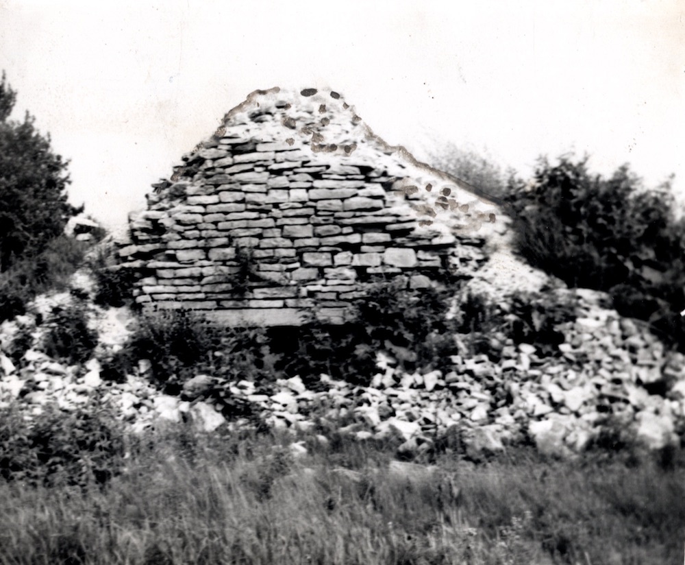 A heap of stone and brick in grass and brush with an opening at the bottom