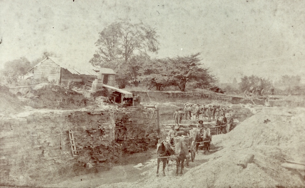 A black and white image of a crew of workers, horses and carts in a quarry pit