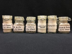 A line of six, labelled glass containers filled with various grits of limestone
