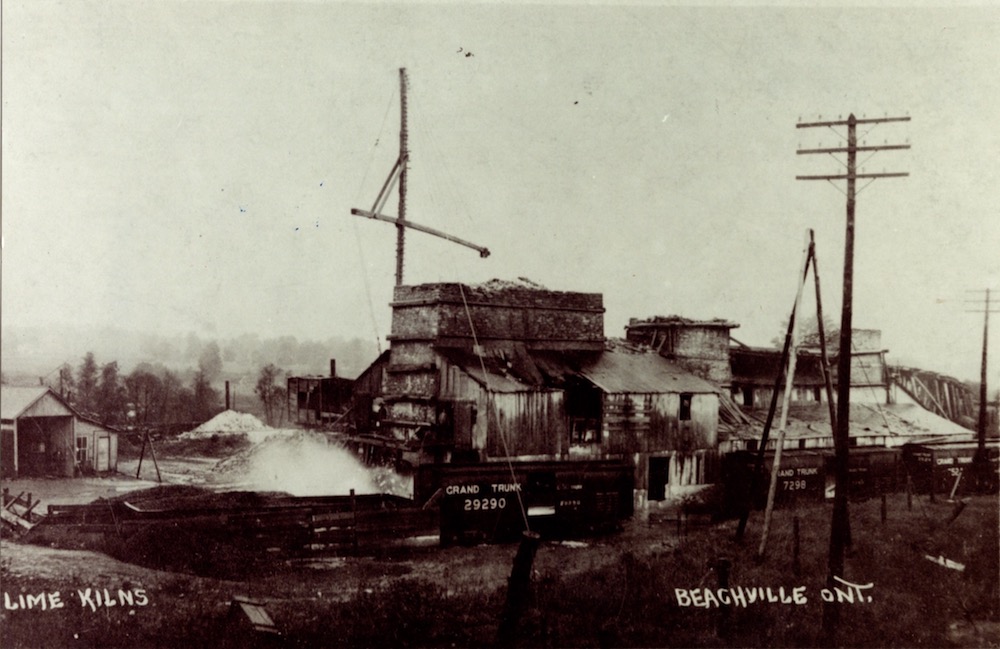 A long set of connected brick and wood buildings beside a railroad track and a hydro pole