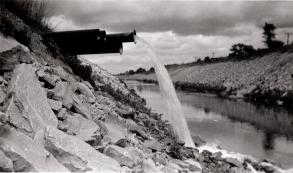  Plusieurs tuyaux noirs sortent d’un tas de pierres et dirigent l’eau vers une rivière en contrebas