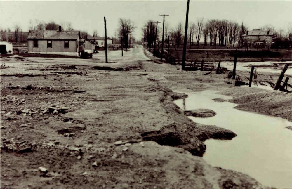 Vue d'une rue inondée avec des flaques d'eau au premier plan et quelques bâtiments sur la gauche