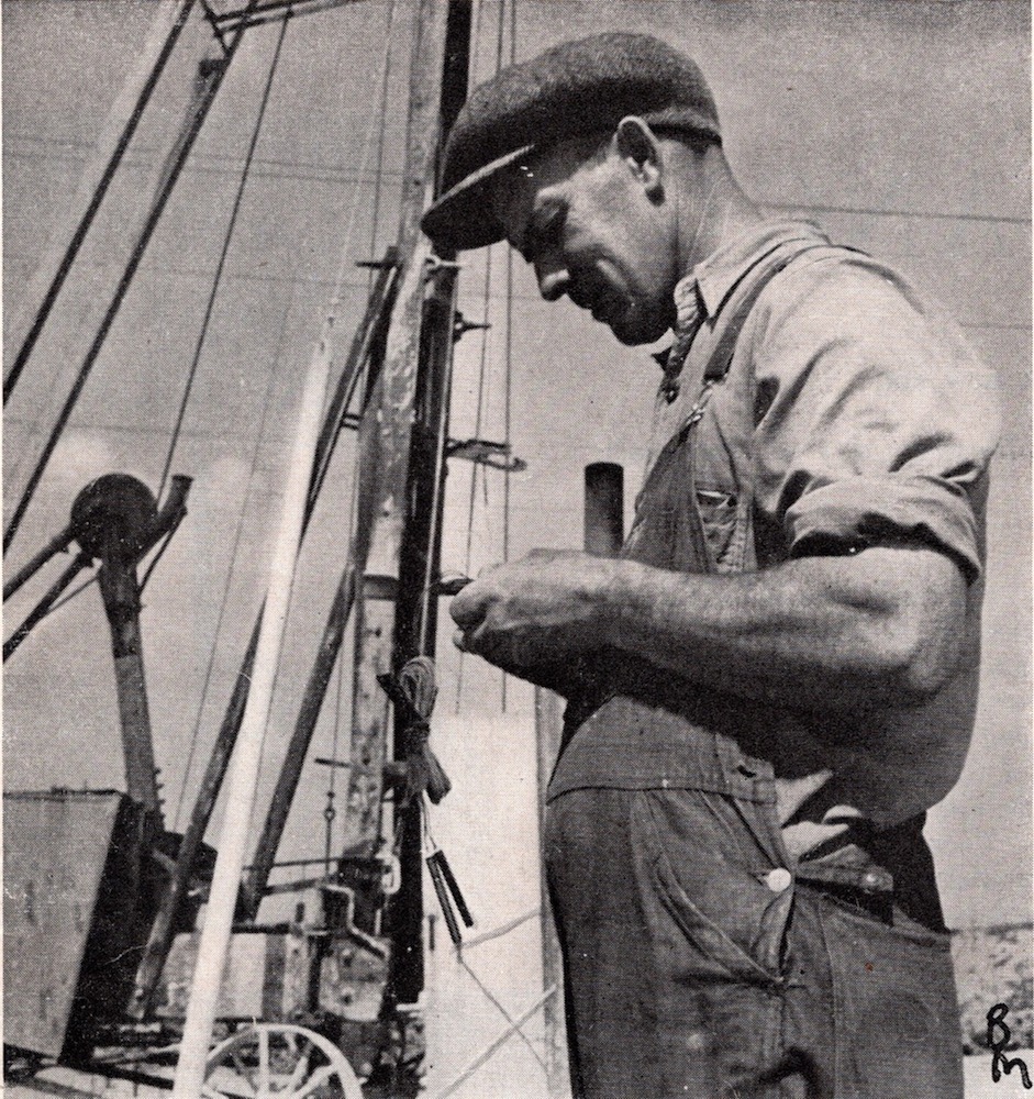 An image from a newspaper clipping showing a man in overalls and a hat holding a detonator