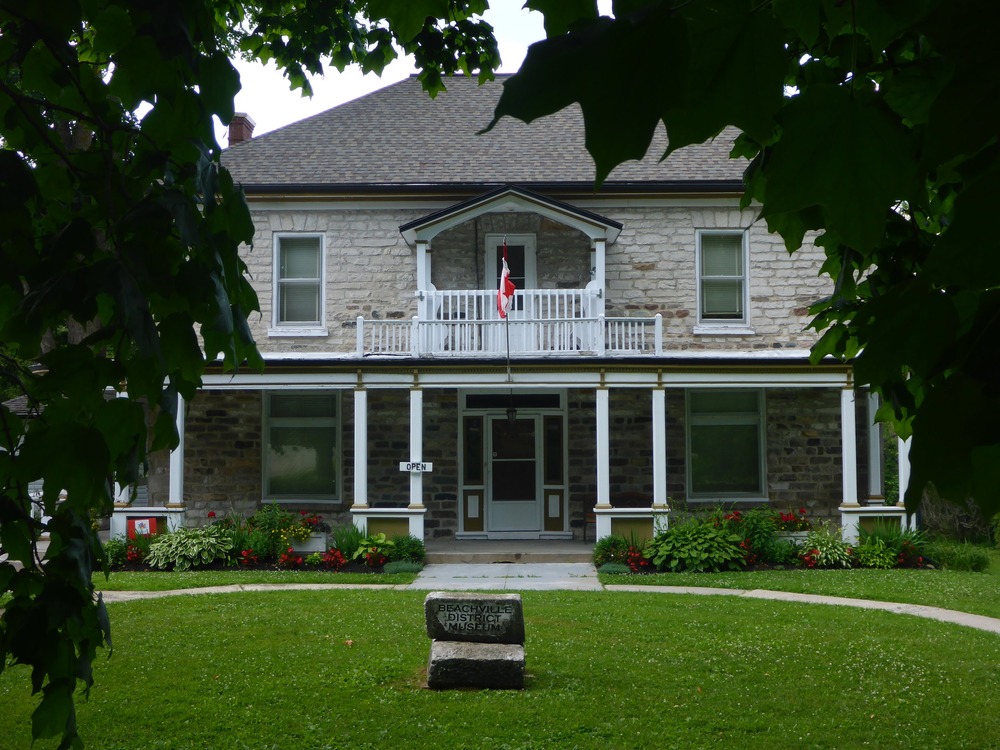 Facade of Beachville District Museum with leaves of trees surrounding the edge of the picture