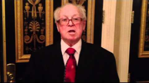 Bingo Hauser in formal attire at an event in 2012 answering questions while being videotaped