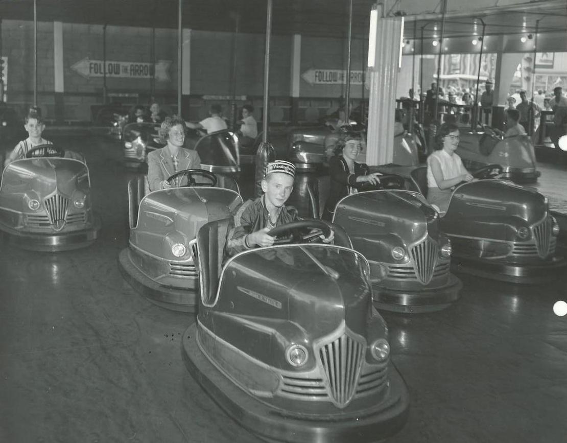 Black and white photo of people riding bumper cars featuring a young boy in front