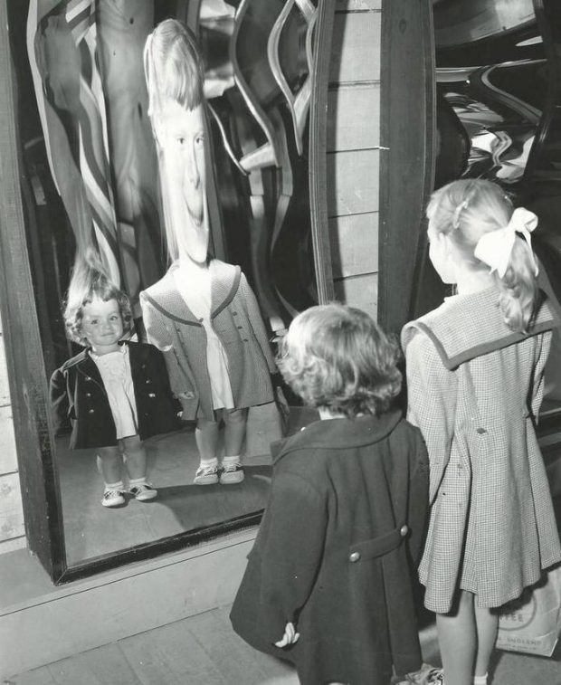 Black and white photo of two little girls looking at their distorted reflections in fun mirrors