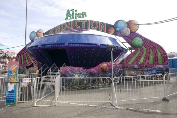 Alien Abduction carnival ride, the ride has a round shape with a big doorway to enter inside, there are colourful lights all over the outside and colourful graphics of outer space along the bottom, the WCA lion mascot is on a sign nearby