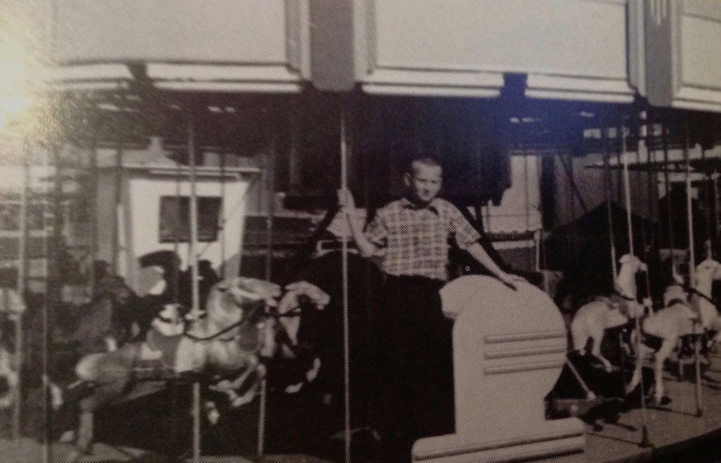 Black and white photo of a young boy posing while standing on a carousel ride