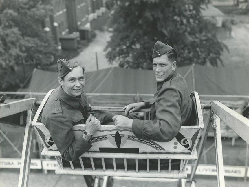Black and white photo of two male soldiers in uniform riding a Ferris wheel, RCA is visible on one of the men's jackets