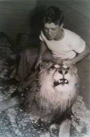 Black and white photo of young Bingo Hauser sitting by his lion, grabbing his mane and tilting his head up slightly