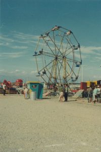 Une grande roue à 12 nacelles et un guichet; en arrière-plan, on aperçoit le manège « Tilt a Whirl », sur le site d’une fête foraine