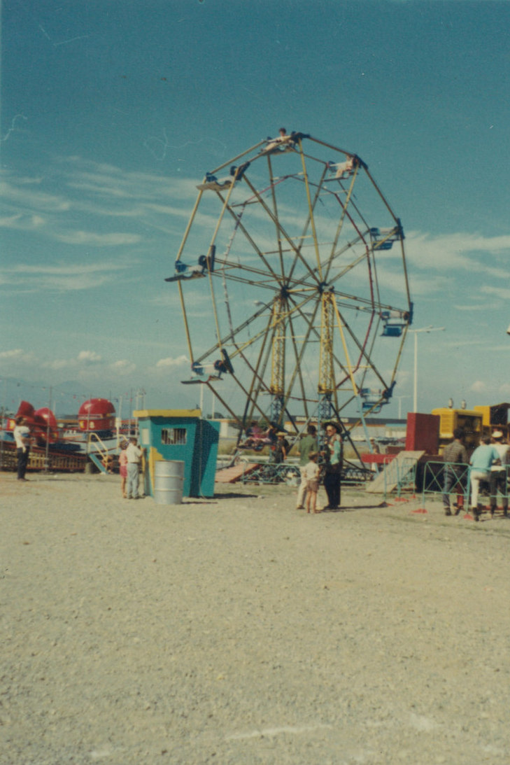 Carnival midway featuring a 12 bucket small Ferris wheel, a ticket sales box and tilt a whirl ride can also be seen