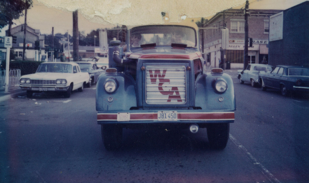 An old fashioned style truck with the letters WCA at the front, driving down a road